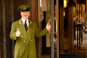 Doorman in green great coat with hat and thumbs up